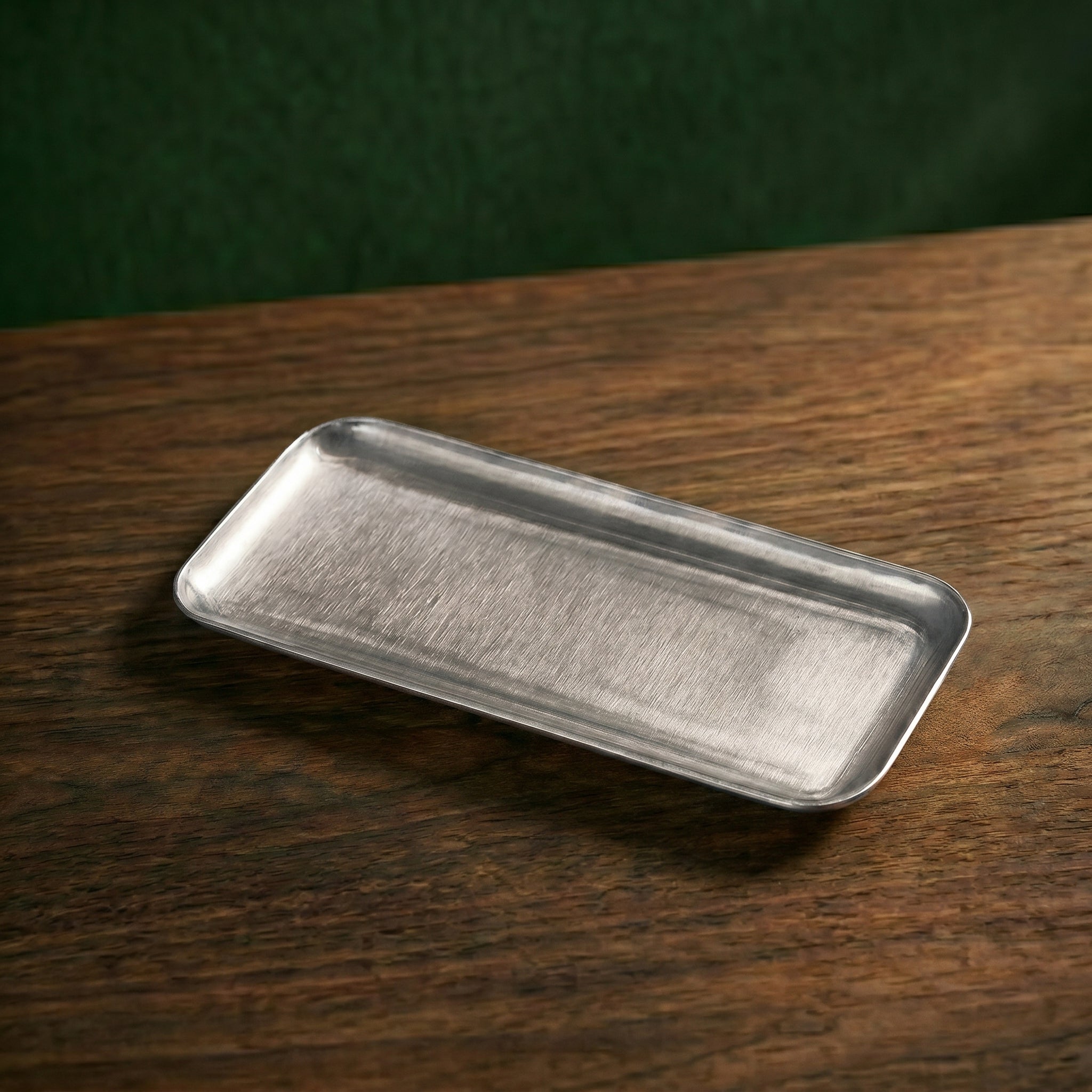 Clean perspective view highlighting the textured, raw industrial brushed grain and curved edges of the narrow rectangular Carson tray on wood.