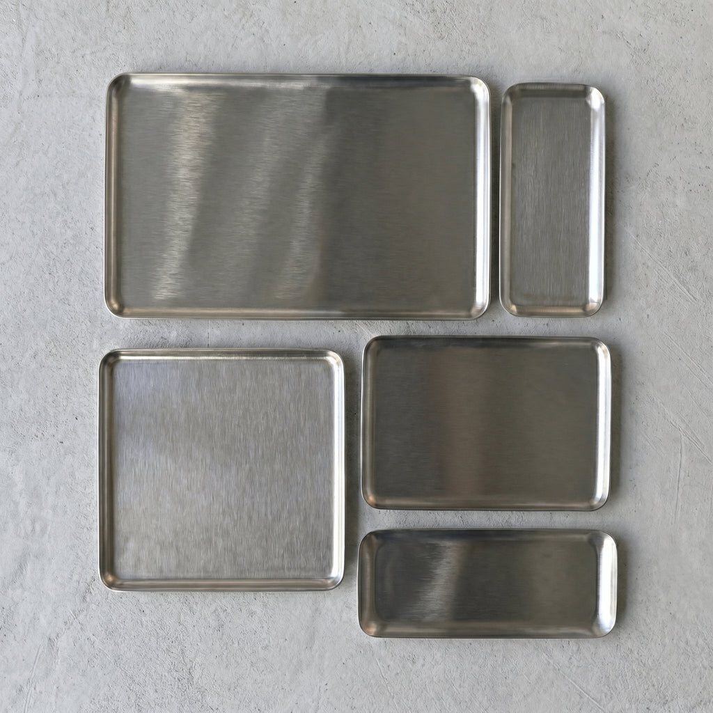 Overhead flat lay documentation displaying five modular sizes and geometric proportions of the Carson brushed stainless steel platters organized on a white textile.