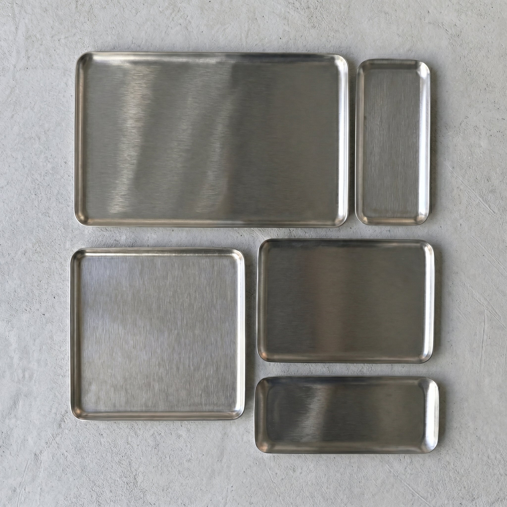 Overhead flat lay documentation displaying five modular sizes and geometric proportions of the Carson brushed stainless steel platters organized on a white textile.