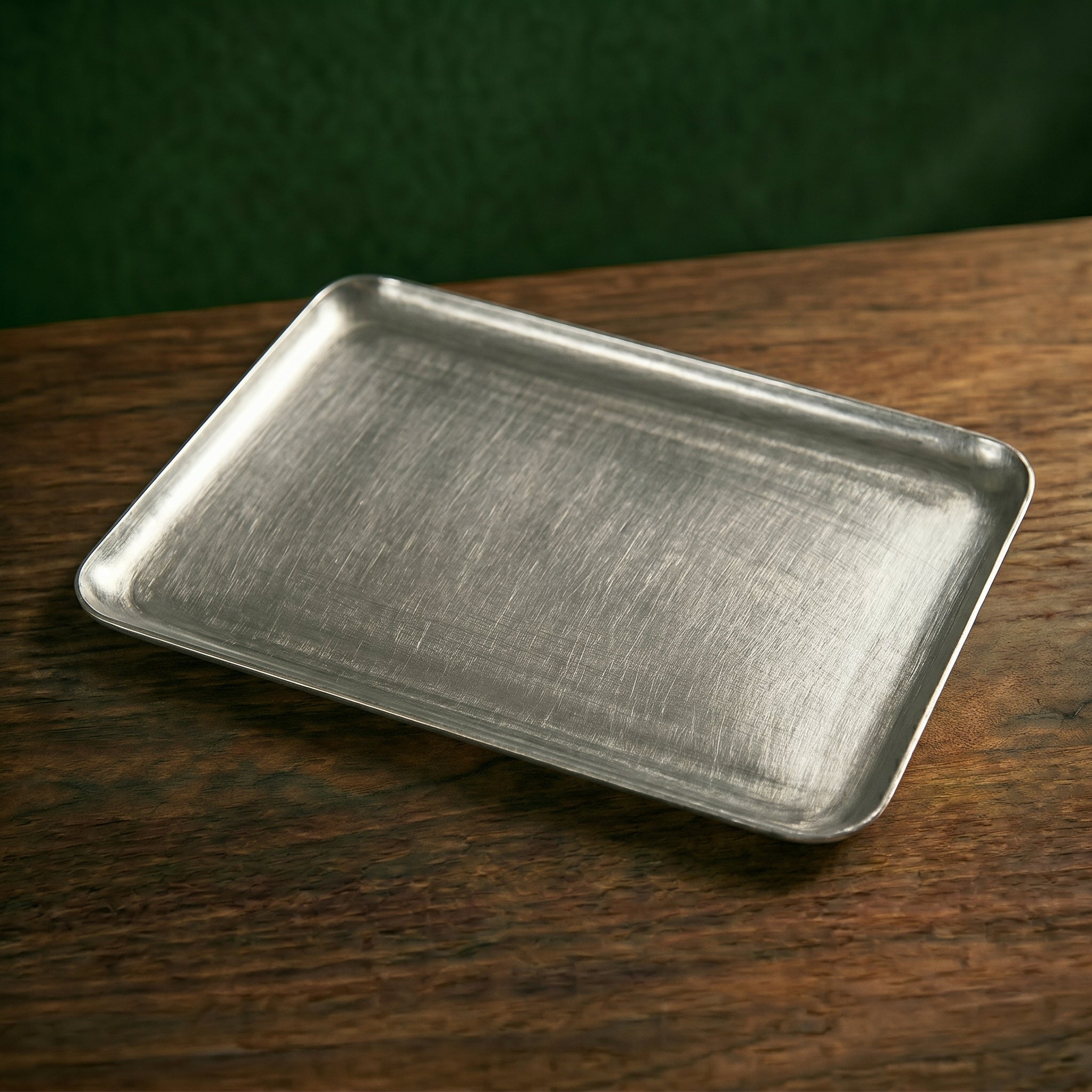 A wide rectangular variant of the Carson brushed steel café presentation platter resting flat on a dark wood tabletop, displaying its textured matte patina.