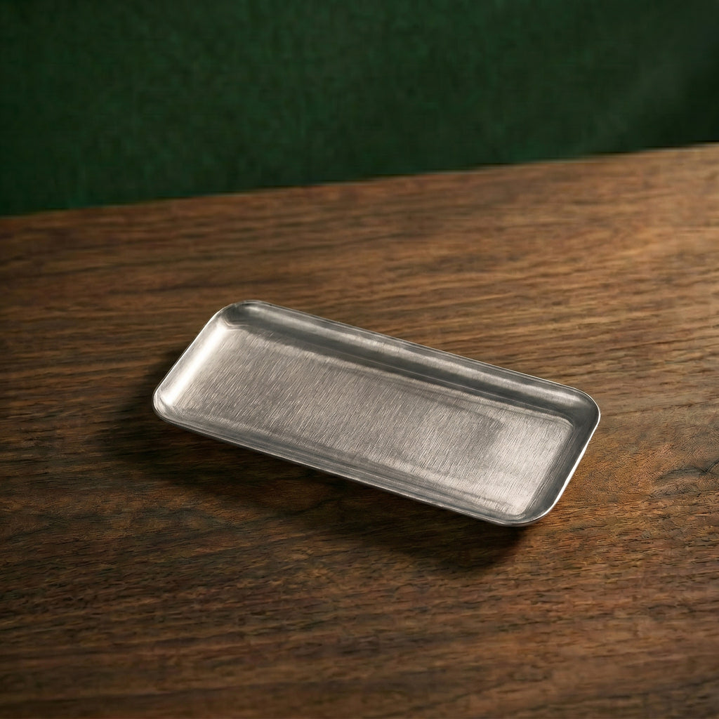 A slender, elongated rectangular variant of the Carson brushed steel presentation platter resting diagonally on a dark timber surface.