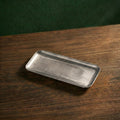 A slender, elongated rectangular variant of the Carson brushed steel presentation platter resting diagonally on a dark timber surface.