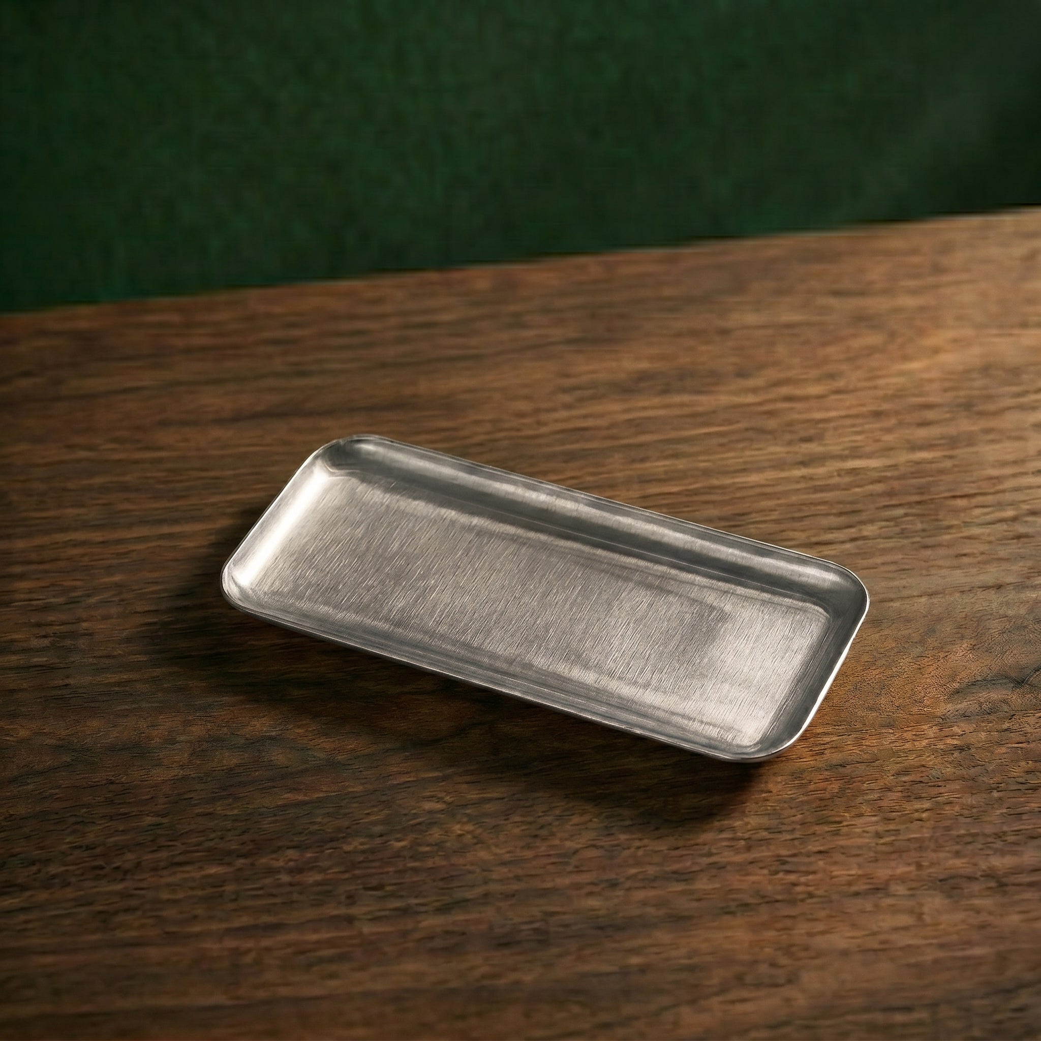 A slender, elongated rectangular variant of the Carson brushed steel presentation platter resting diagonally on a dark timber surface.
