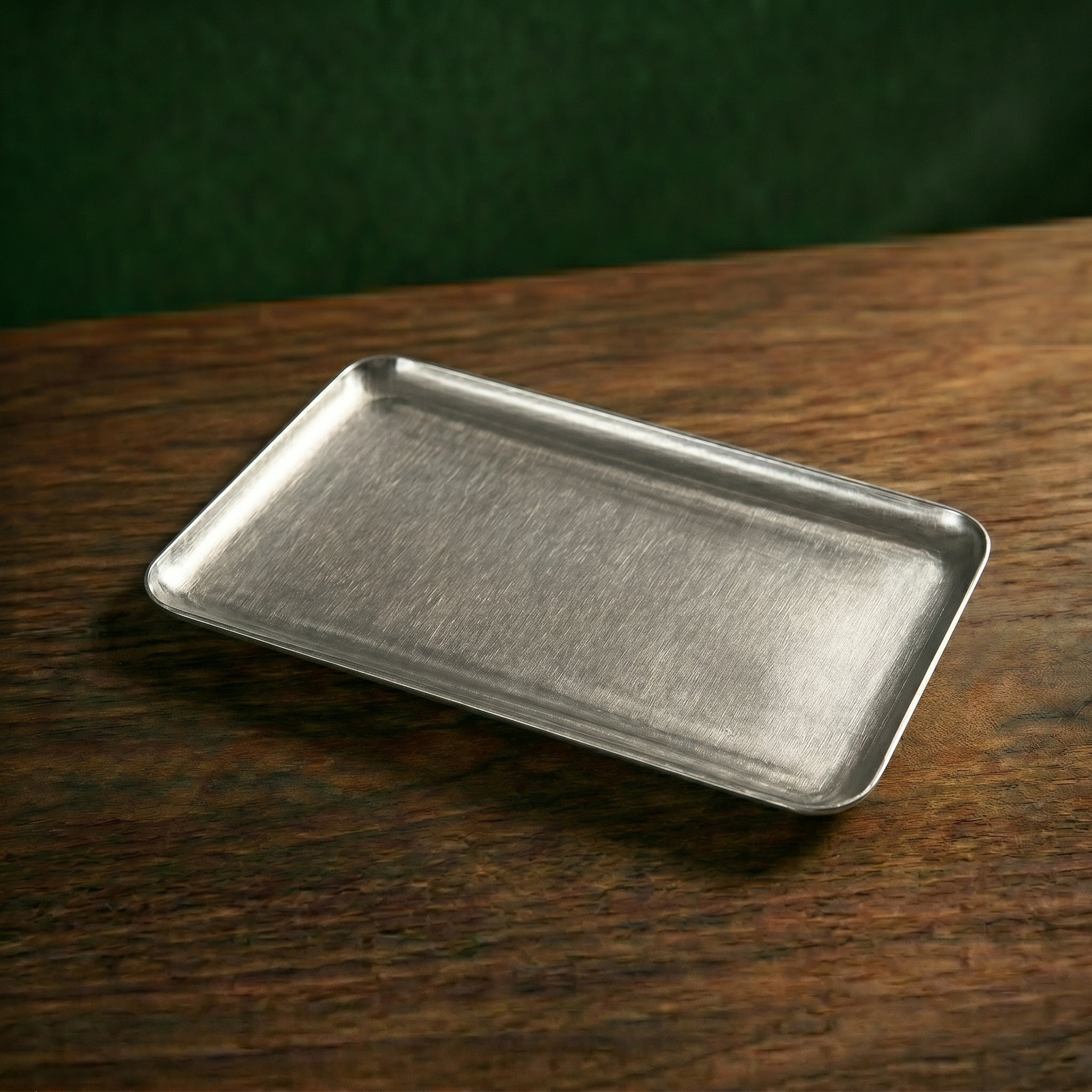 A medium rectangular Carson brushed steel serving tray resting flat on a dark timber countertop under focused café ambient lighting.