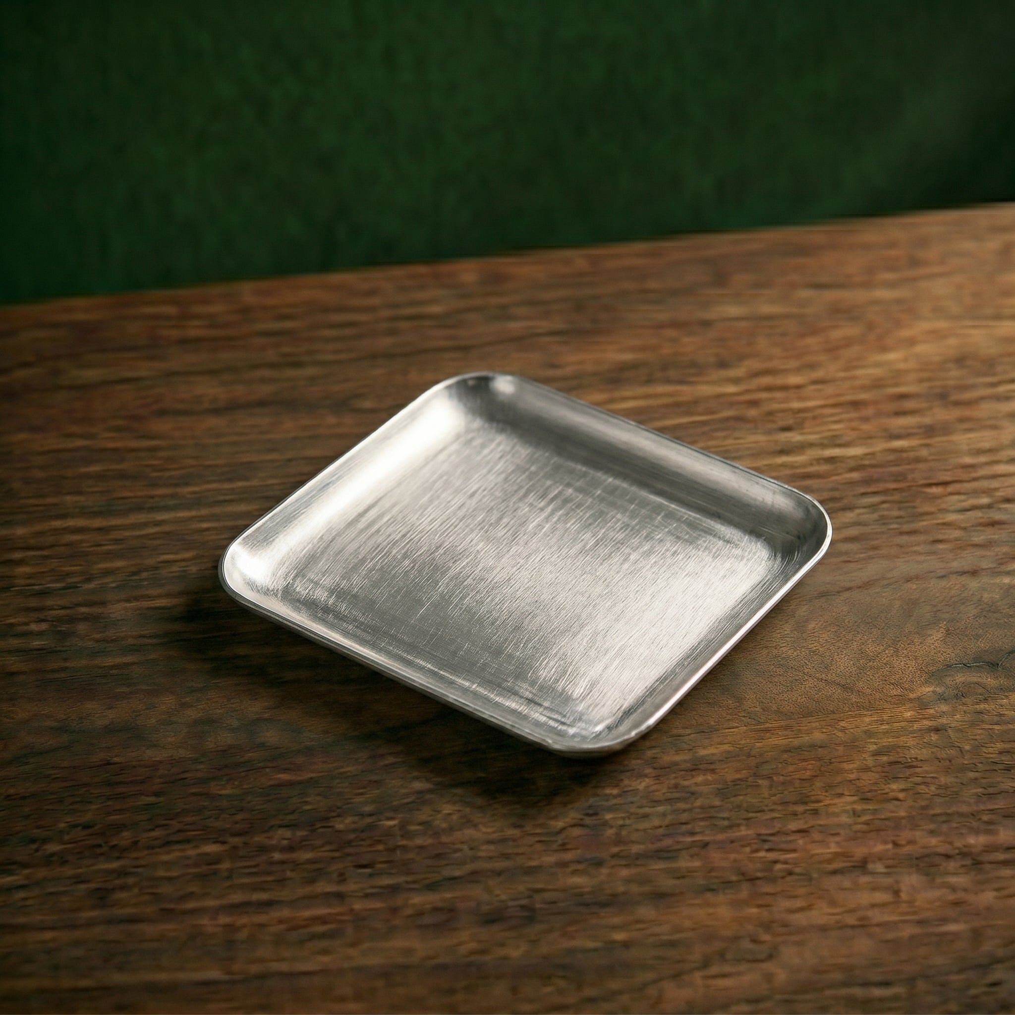 A compact, square-profile variant of the Carson brushed service platter resting on a dark wood counter, optimized for single espresso or bakehouse servings.