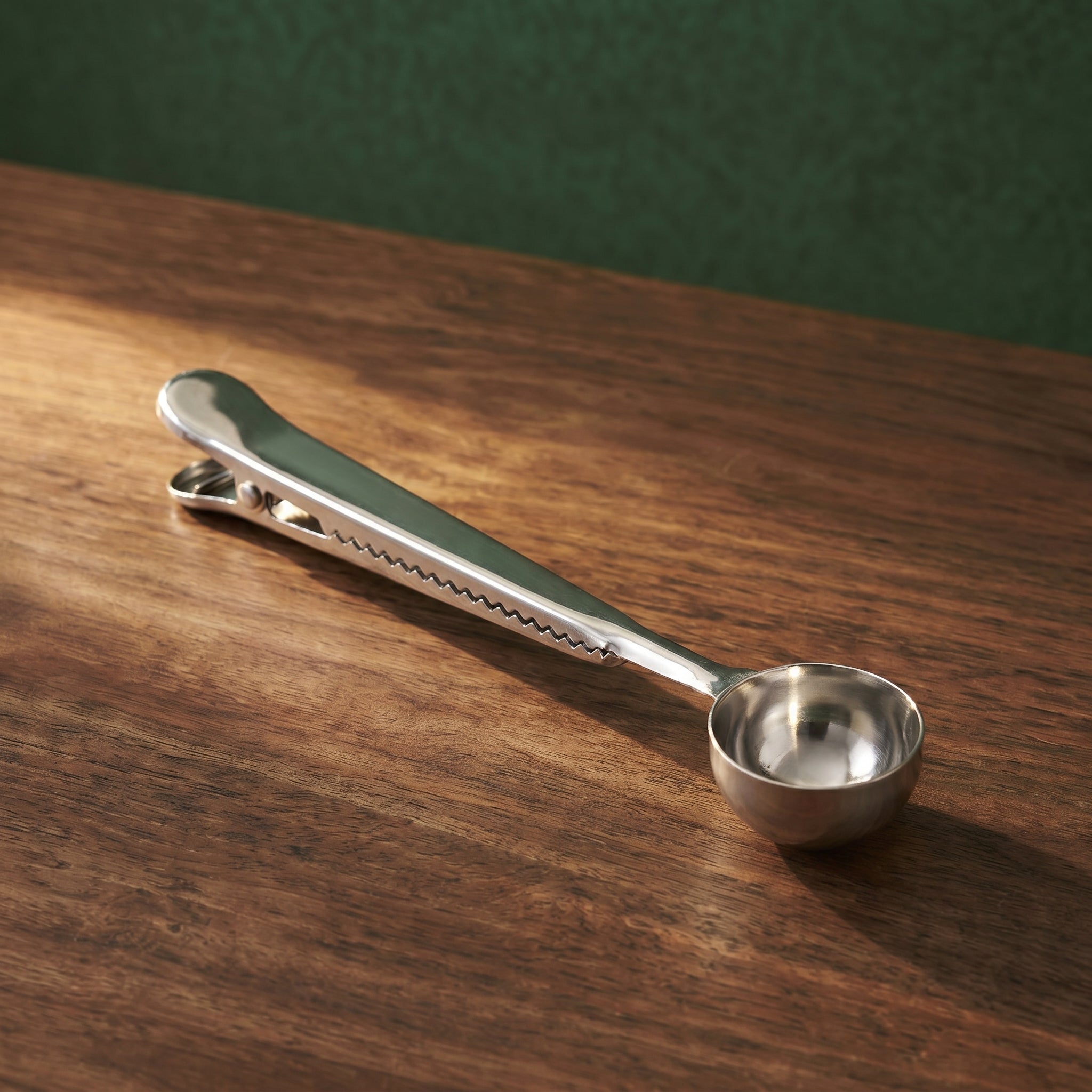 The polished chrome silver variant of the Dalton tapered scoop and clamp resting diagonally across a dark timber counter under soft lighting.