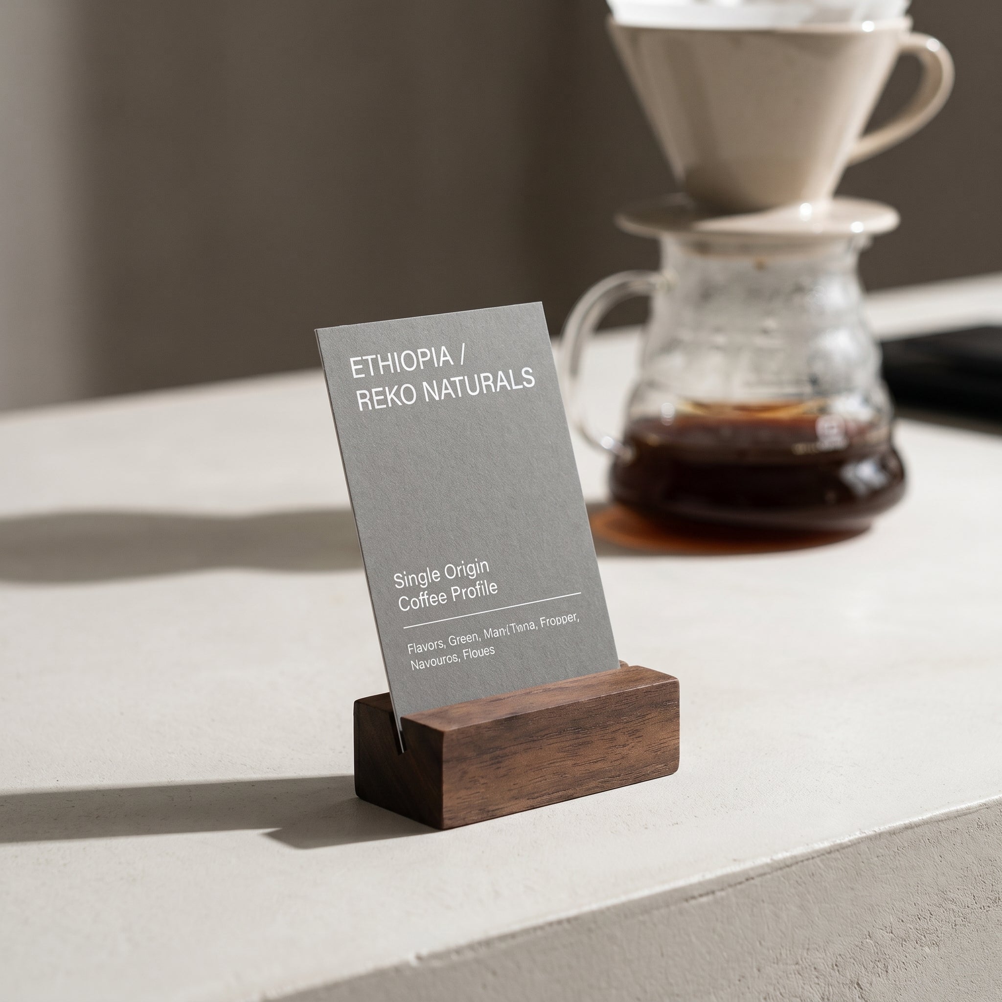 The Radcliffe walnut menu block holding a vertical grey informational card next to a clear glass pour-over coffee carafe on a stone brew bar workstation.