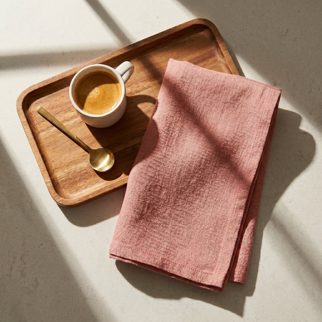 The Sutton stonewashed linen napkin in ochre pink resting on a cafe presentation tray with a warm espresso cup setup.