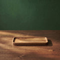 Small Vance beveled walnut wood tray displayed on a wooden tabletop against a textured dark green background, showcasing its slim profile for cafe or restaurant service.