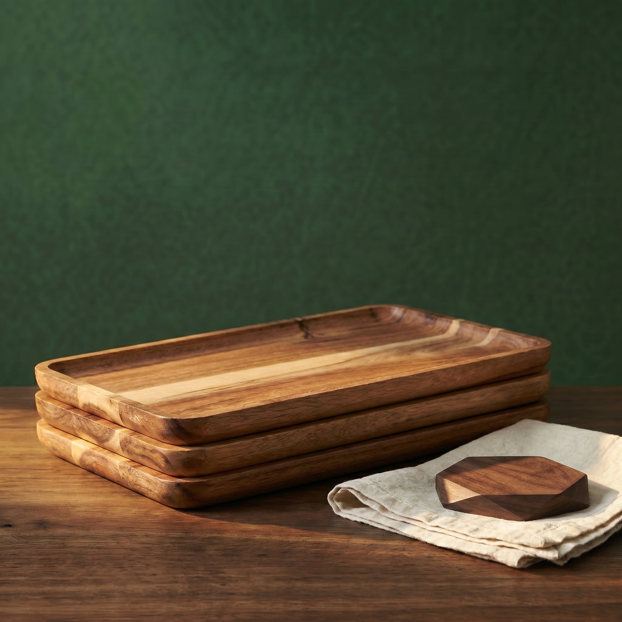 A structural stack of four modular Vance rectangular wood trays resting on a walnut counter next to a linen cloth and a geometric timber coaster.